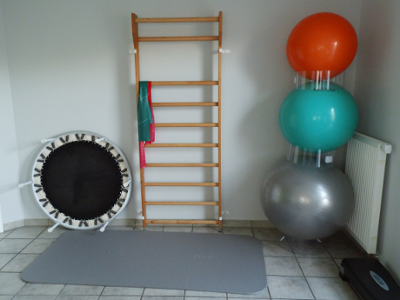 Der groe Behandlungsraum: auf dem Boden liegt eine Turnmatte, an der Wand steht eine Sprossenwand, links davon ein Trampolin und rechts in der Ecke drei aufeinander gestapelte Gymnastikblle.